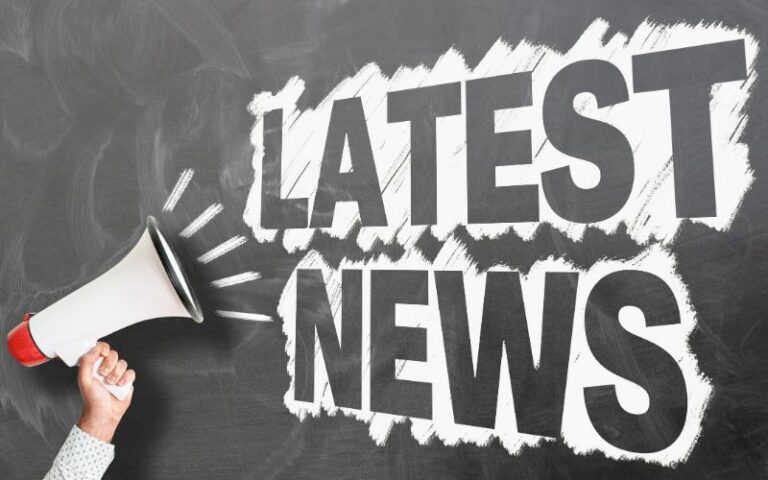 A hand holding a bull horn with "Latest News" written on a dark chalkboard